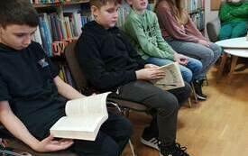 Czworo dzieci siedzi na krzesłach, dwoje z nich trzyma otwartą książkę w rękach i czyta.