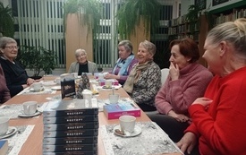 Siedem kobiet siedzi przy stole i rozmawia, na stole leżą książki o kt&oacute;rych toczy się rozmowa
