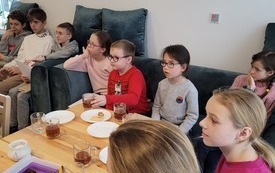 dziewczynki i chłopcy siedzą na kanapach i słuchają z zaciekawieniem, osoby, która do nich coś mówi.