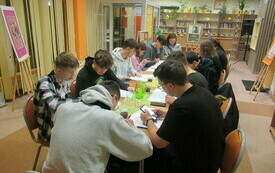 Grupa młodzieży siedząca przy stole rozwiązuje zadania konkursowe. 
