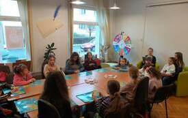 Grupa dzieci siedzi wok&oacute;ł stołu, na blacie leżą kolorowe plansze
