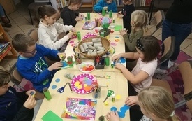Grupa dzieci siedzi wok&oacute;ł stołu z artykułami papierniczymi