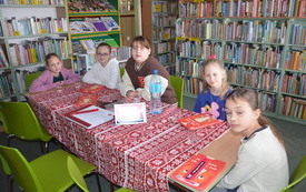 Pięć dziewczynek siedzi przy stole, jedna z nich ma zamknięte oczy. W tle regały z książkami.