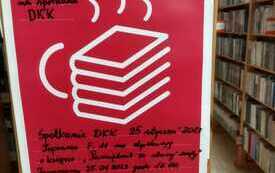 Plakat Dyskusyjnych Klub&oacute;w Książki, prezentujący stos książek, ustawionych w kształcie filiżanki. W tle regały z książkami.