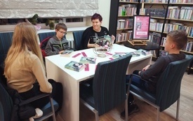 Troje dzieci i kobieta siedzą przy stole, w tle regały z książkami.
