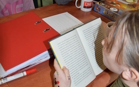 Troje dzieci siedzi przy stole, dziewczynka ma otwartą książkę.