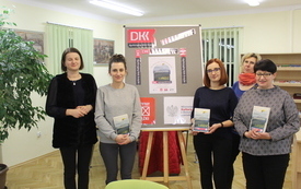 Cztery kobiety stoi i trzyma w rękach książkę, w tle plakat Dyskusyjnych Klubów Książki.