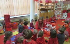 Grupa ubranych na czerwono dzieci siedzi na czerwnym dywanie w bibliotece