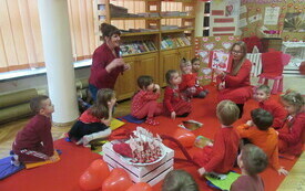 Grupa ubranych na czerwono dzieci siedzi na czerwnym dywanie w bibliotece