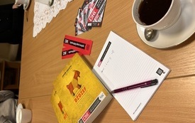 Na stole książka, kawa w filiżance i materiały z logo DKK.