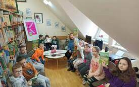 Kilkoro dzieci siedzi przy stoliku w k&oacute;łeczku. Niekt&oacute;re z nich pokazują książkę, kt&oacute;rą omawiają. 