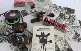 Na stole leżą stare fotografie, książka, aparat fotograficzny i klisze. 
