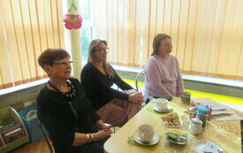 Trzy kobiety w średnim wieku siedzące przy stoliku kawowym patrzące przed siebie.