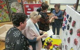 Uczestnicy spotkania oglądający broszki i ozdoby biżuteryjne wykonane przez gościa spotkania.