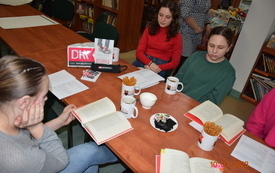 Kilka dziewczyn siedzi przy stole i rozmawia o książce.