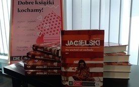 Dwa stosy książek na stole, w tle plakat Dyskusyjnych Klubów Książki.
