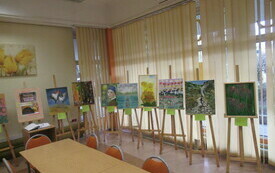 Widok na salę wystawienniczą z rzędem sztalug z obrazami