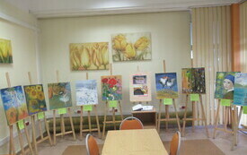 Widok na salę wystawienniczą z rzędem sztalug z obrazami