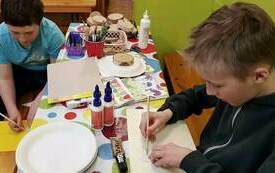 Dzieci siedzą przy stole i wykonują pracę plastyczną. 