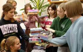 Kilkanaście dzieci stoi wok&oacute;ł stosu książek. 