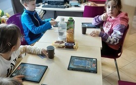 Czworo dzieci siedzi przy stole, książki leżą na stole.