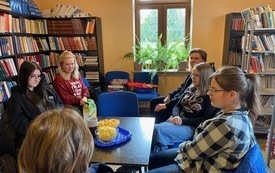 Grupa nastolatków siedzi wokół stołu i rozmawia. Na stole leżą książki.