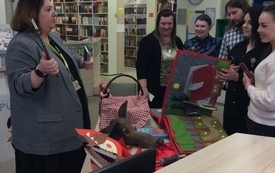 Cztery kobiety i jeden mężczyzna oglądają książkę wykonana z filcu. Obok książki leży koszyk czerwonego kapturka, głowa wilka. 