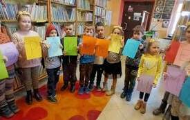 Grupa dzieci trzyma kartki papieru z literami, kt&oacute;re układają się w napis WSP&Oacute;ŁPRACA. 