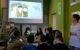Dzieci siedzą i oglądają film wyświetlany na ekranie.