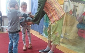 Aktor w kolorowym stroju wręcza dw&oacute;jce dzieci rekwizyty
