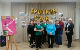 Kilka kobiet stoi przy sztaludze z plakatem DKK. W tle napis: Spotkań czar.