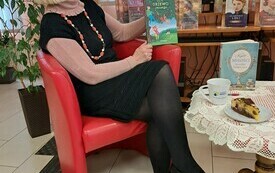 Kobieta w okularach siedzi w fotelu, w ręku trzyma książkę Drzewko Jessego&quot;.