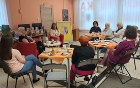 Uczestniczki spotkania, kobiety siedzą przy stolikach kawowych wpatrzone w autorkę i prowadzącą spotkanie. 