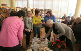Uczestnicy spotkania zebrani wok&oacute;ł stolika z porcelanowymi naczyniami. Kobiety oglądają naczynia. 