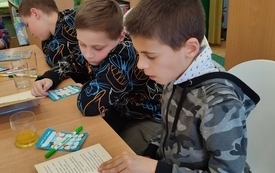 Trzech chłopców siedzi przy stole i przegląda książkę.