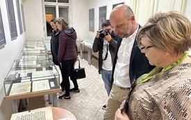 Prezydent Rzeszowa ogląda rozłożoną na stoliku książkę ze zbior&oacute;w Biblioteki. Obok kobieta i mężczyzna robiący zdjęcia.