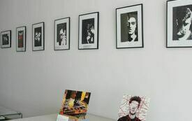 Na ścianach wiszą czarno białe obrazy przedstawiające postać mężczyzny. Poniżej na stoliku stoją dwie prace na sztalugach. 