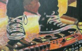 Obraz przedstawiający nogi w czarnych spodniach i trampkach. Jedna noga dotyka miksera muzycznego.