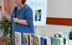 Na zdjęciu autorka mówi do mikrofonu, na stoliku książki.