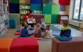 Kilka dzieci siedzi na dywanie i patrzą na prowadzącą spotkanie.