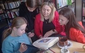 Kilka osób ogląda rozłożoną na stoliku książkę.