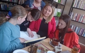 Kilka osób ogląda rozłożoną na stoliku książkę.