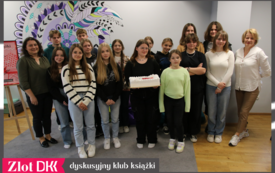 Grupa młodych ludzi stoi, dziewczyna trzyma tort z logo Dyskusyjnych Klubów Książki.