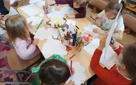 Dzieci siedzą wokół stolika i wykonują laurki dla mamy
