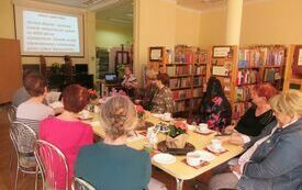 Kobiety siedzące przy stole patrzą na ekran projekcyjny, na którym wyświetla się prezentacja o Wielopolu Skrzyńskim.