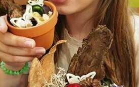 Dziewczynka trzymająca w ręku poidełka dla pszcz&oacute;ł wykonane z mchu, szyszek, kory i innych ekologicznych element&oacute;w. 