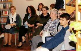 Uczestnicy spotkania siedzą na krzesłach. Wokół regały z książkami.