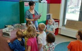 Kobieta opowiada coś dzieciom, które stoją i patrzą.