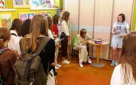Gość spotkania, młoda kobieta w okularach w trakcie rozdawania autograf&oacute;w. Obok kolejka młodzieży czekająca na autograf.