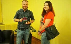 Pisarz, Wojciech Chmielarz trzyma w rękach swoją książkę. Obok stoi młoda dziewczyna i uśmiecha się.